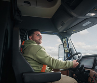 Professional truck driver operating Freightliner semi truck, side profile view from cab interior